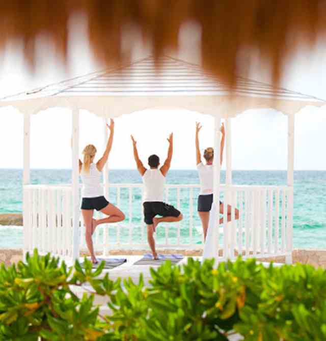 Calm yoga group training in tree pose meditating by ocean sea at Karisma Hotels & Resorts®